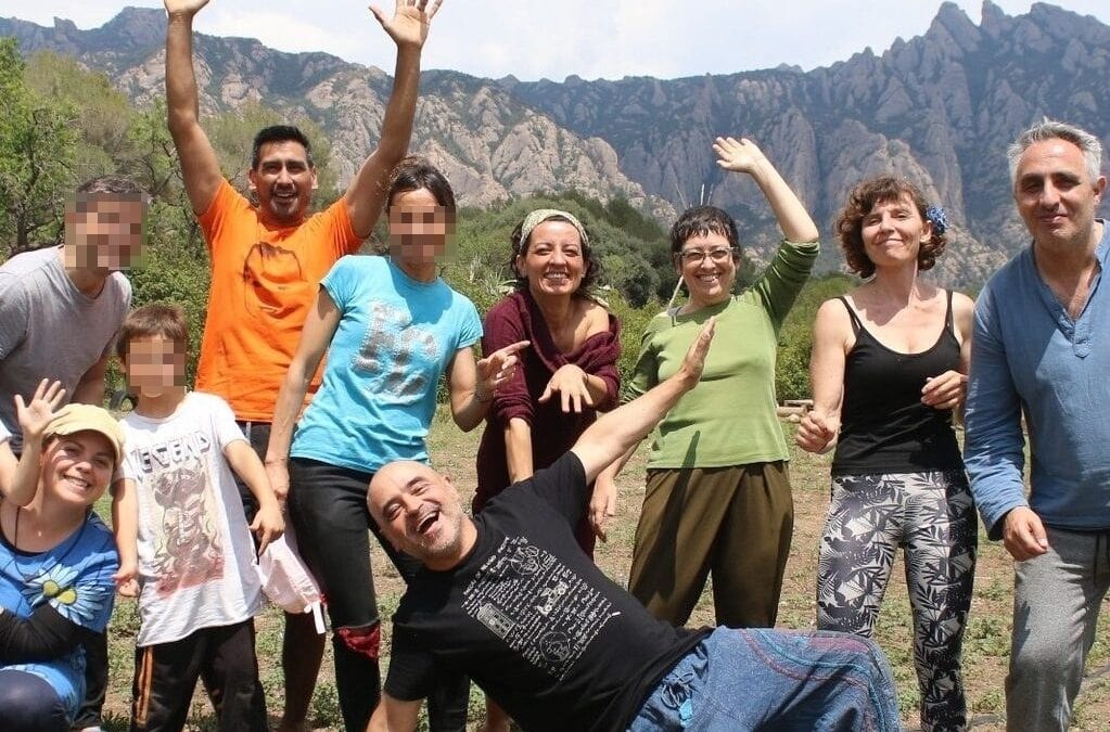 Un grupo de diez personas, entre las que hay niños con la cara borrosa, posan y sonríen al aire libre con las montañas de fondo.
