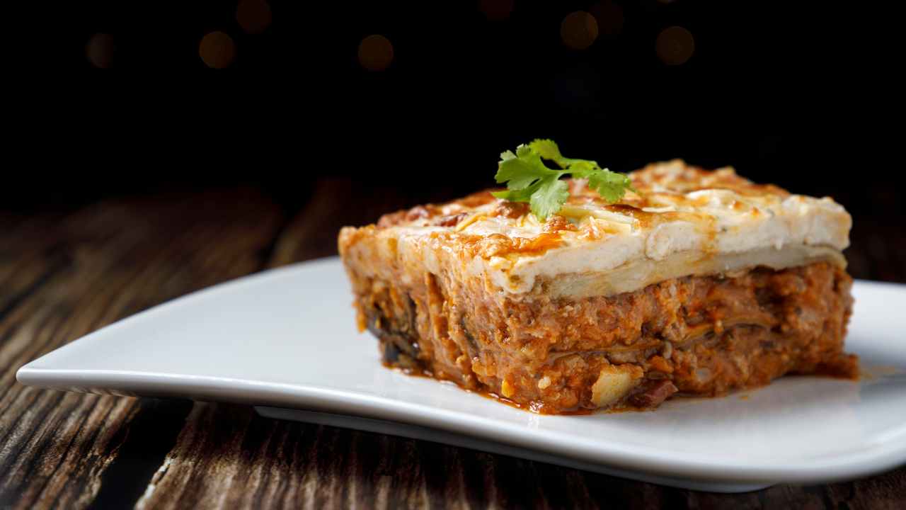 destacadas blog musaka una porción de musaka en un plato blanco sobre una mesa de madera