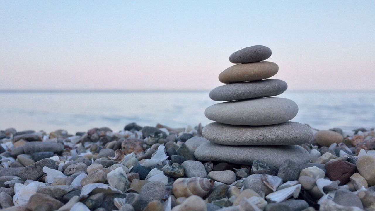 dilo en 40 palabras fotografía que muestra una pequeña pila de piedras lisas y planas en una playa al atardecer